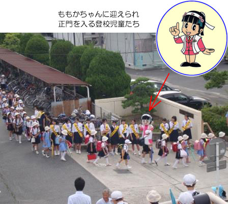 ももかちゃんに迎えられ正門を入る登校児童たち ももかちゃんに迎えられ正門を入る登校児童たち