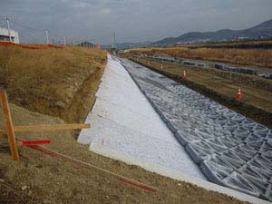 削られた法面に敷かれた遮水シートの上に並べられた護岸ブロック 削られた法面に敷かれた遮水シートの上に並べられた護岸ブロック